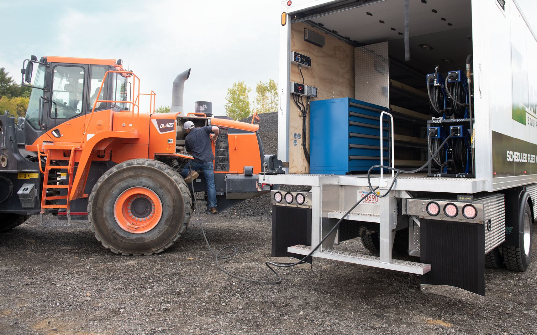 A heavy equipment service technician performs work in the field using a mobile lubrication truck.
