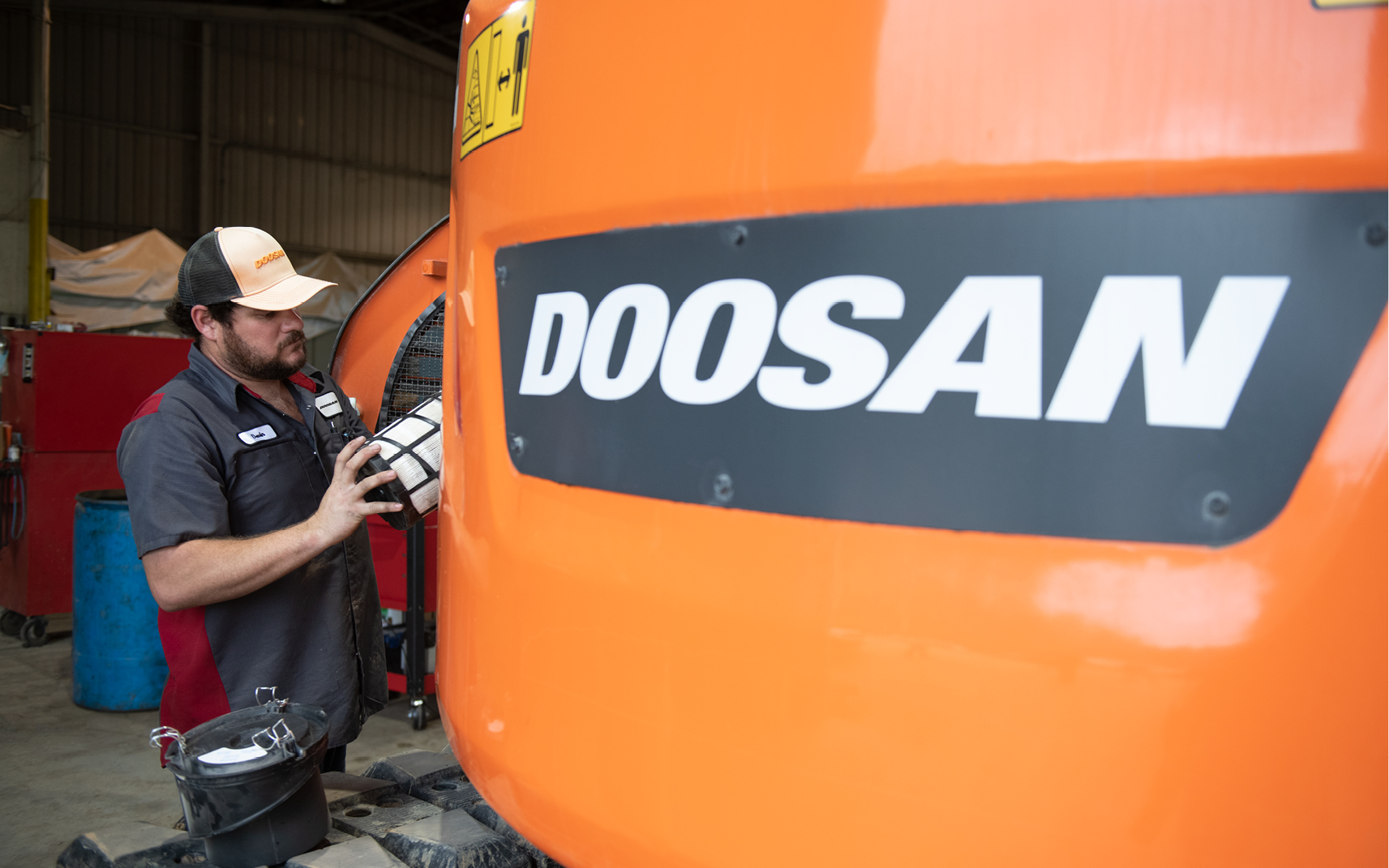 A service technician replaces a filter in a Doosan crawler excavator.