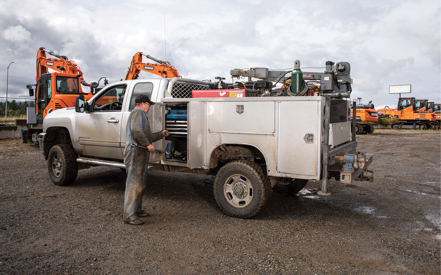 A heavy equipment service technician retrieves tools from his field service truck and performs maintenance at a jobsite.