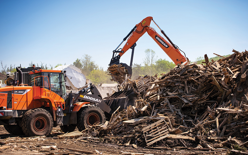 A Doosan wheel loader and crawler excavator work in tandem to lift and sort wood waste at a New Jersey recycling facility.
