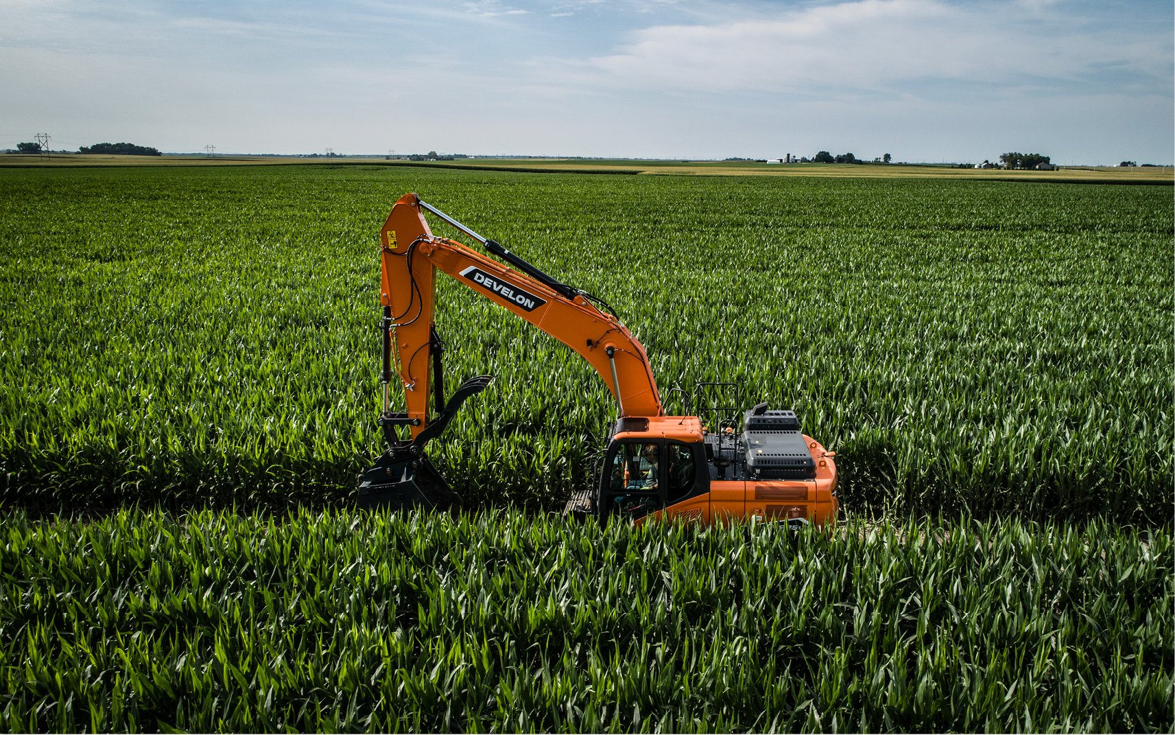 A drone image of a DEVELON excavator moving through a cornfield.